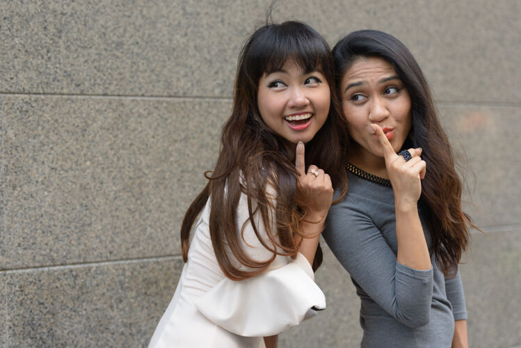城市两位年轻的亚洲女商人在城市户外的合影市中心手势女同性恋