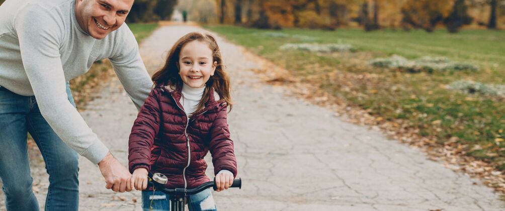 童年可爱的小女孩和她爸爸在公园里学骑自行车快乐父亲女儿