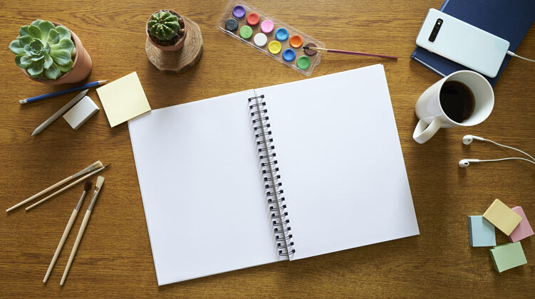 打开笔记本木制桌面与水彩画工具 一个打开的笔记本 和刷子木制桌面水彩顶视图