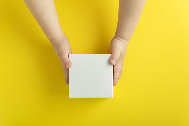 儿童儿童手中的白色纸板箱 黄色背景.top查看.复制空间 模型手包装纸张