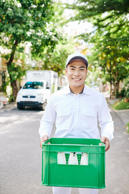 男性正面的亚洲送货员拿着塑料箱和玻璃奶瓶携带盒子乳制品