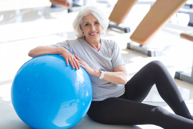 放松生活就是太好了满意了漂亮的老太太坐在地板上 一边笑一边把胳膊放在健身球上减肥健身老年人