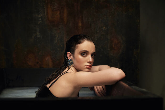 时尚侧视图湿黑发女孩坐在黑色浴缸与泥泞的白水银色浴缸黑色
