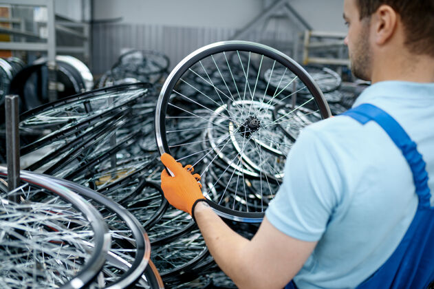 金属穿制服的技工把自行车轮子放在地上工厂自行车轮缘和辐条在车间组装 循环零件安装自行车运输辐条