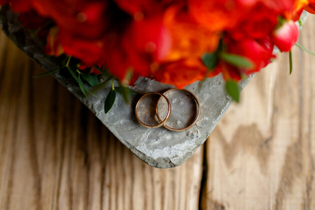 叶木制背景上的结婚戒指和一束鲜花花瓣戒指珠宝