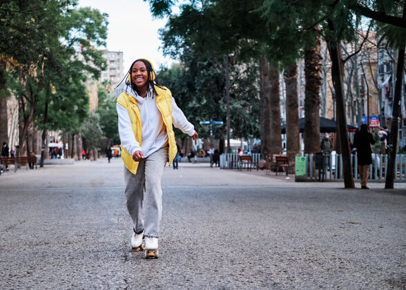 耳机一位非洲裔美国妇女在户外滑冰时微笑着 戴着耳机听音乐街道.城市概念城市欢呼女性