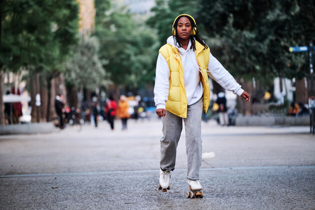 活动一位非洲裔美国妇女在户外玩旱冰时戴着耳机听音乐街道.城市概念溜冰非洲裔美国人民族