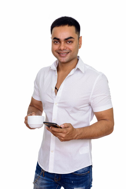 信息年轻快乐的印度男人一边拿着咖啡杯一边用手机男人20多岁短信