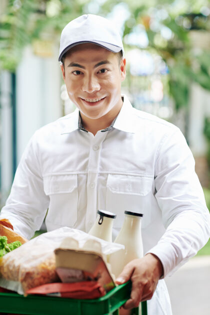 亚洲微笑的越南信使运送新鲜的产品 如牛奶 鸡蛋和面包塑料箱男人商店新鲜