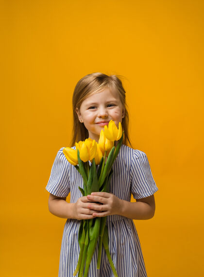 女性一个微笑的小女孩的肖像 黄色的郁金香上有一束黄色的郁金香脸黄色礼服