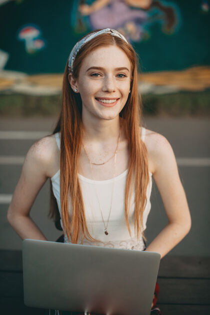 户外一位美丽的红发学生的画像 她课后坐在公园里 腿上放着一台笔记本电脑 微笑着工人无线学习