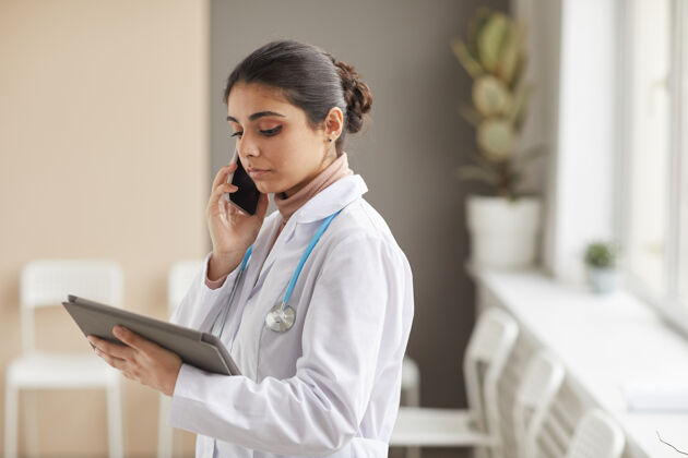 工作身穿白大褂的女医生站在医院里用手机聊天 看着手里的数码平板电脑站立信心职业