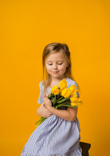 拥抱一个漂亮的金发女孩穿着条纹连衣裙坐在那里 看着一束黄色的郁金香幼儿束黄色