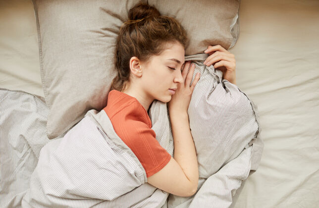 早晨高角度拍摄的年轻女子躺在枕头上闭着眼睛睡觉 床上放着毯子午睡成人卧室