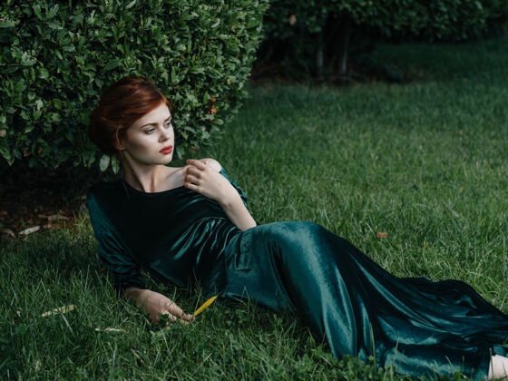吸引力身着绿色连衣裙的美女躺在绿色的灌木草地上自然奢华的模特模型衣服金发