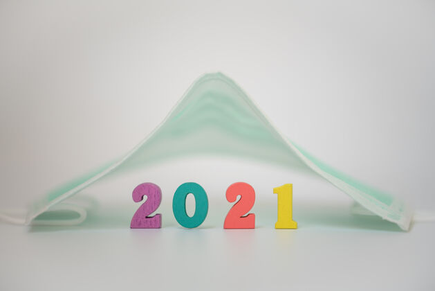 假日2021年新年 covid-19和helathcare概念特写白色背景上的手术面罩下面的木制彩色数字日愿望事件