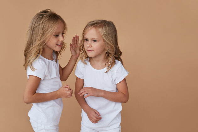 金发一对可爱的小双胞胎姐妹的正面特写肖像 金色卷发 互相交谈 穿着白色衣服姿势可爱童年