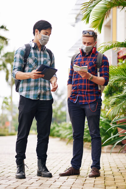 防护面罩年轻人戴着医用口罩迷失在城市里查看纸质地图和在线导航应用程序亚洲人谈话旅行