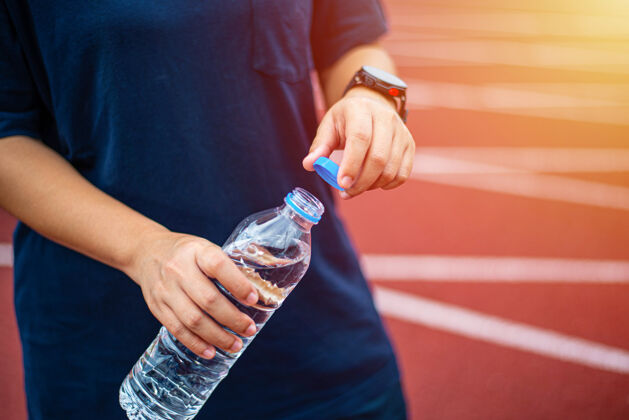 饮用运动员在跑道上用手打开水瓶热清洁健身