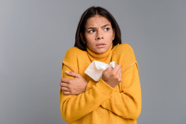 胳膊一个冻坏了的女人拿着餐巾孤立地站在灰色的墙上毛衣疾病鼻子
