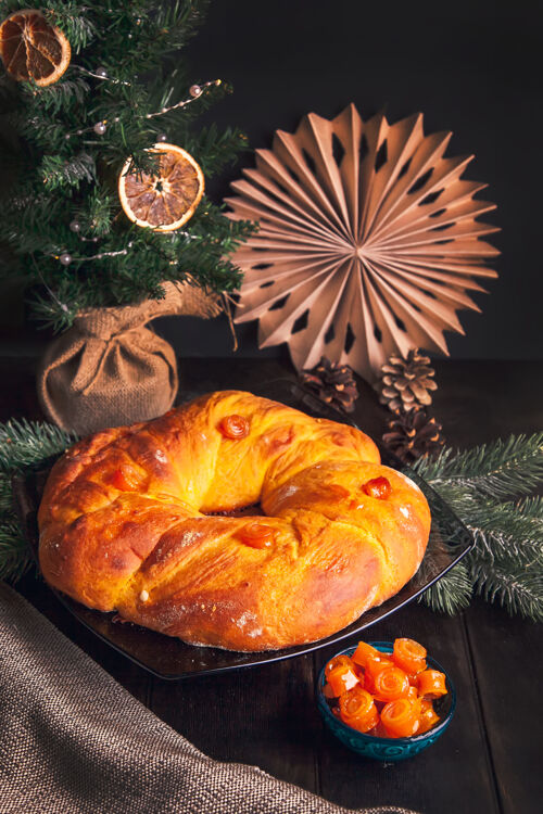 烘焙在圣诞树的背景上 家庭烘焙的圣诞面包形状是酵母面团和橙色蜜饯水果做成的花环装饰糕点乡村风味