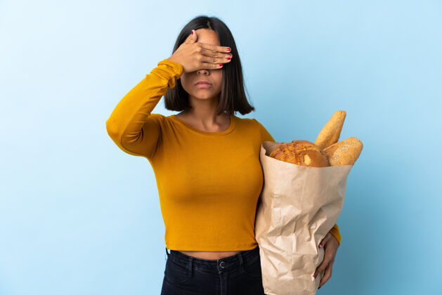 眼睛一个年轻的拉丁女人在买面包 她用蓝色圆锥形的眼睛看面包手.do不想看到什么表情手势吃