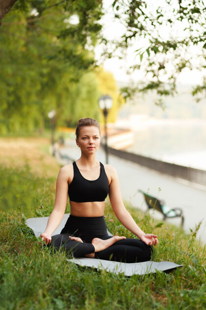 公园正面图片：一名年轻女子练习瑜伽 坐在莲花姿势 穿着运动服在冥想会议上垂直停车查看女人姿势瑜伽