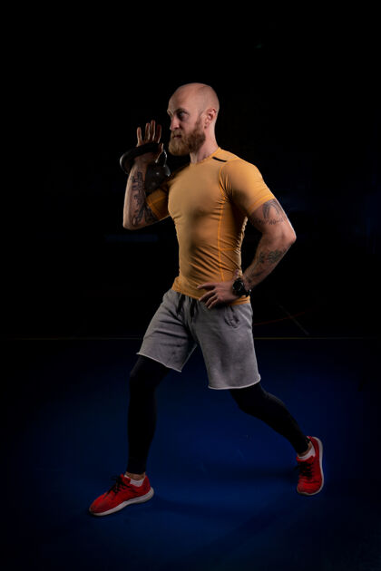 肌肉留着胡子的纹身运动员准备用一只手举起壶铃健身室内体重