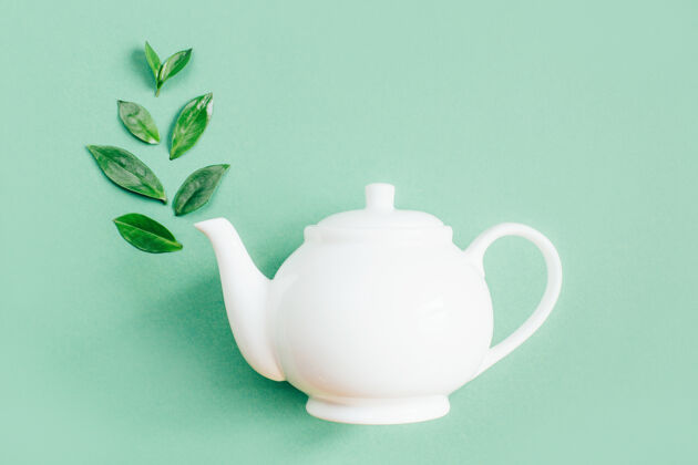 白茶壶绿色表面上白色茶壶和茶叶的俯视图绿色容器草药