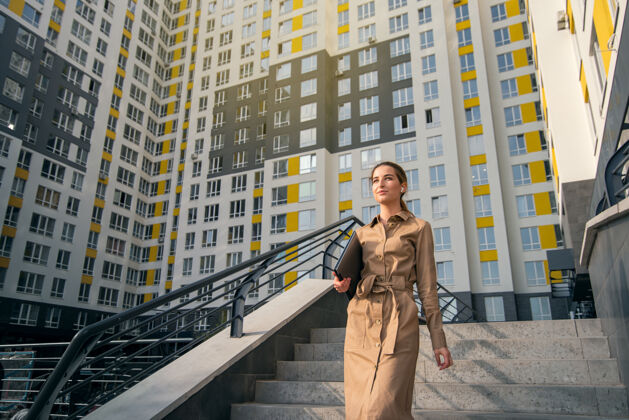 阳光一个穿着休闲服的年轻女子拿着一台笔记本电脑走下一座高楼的楼梯建筑业城市生活理念休闲职业女性