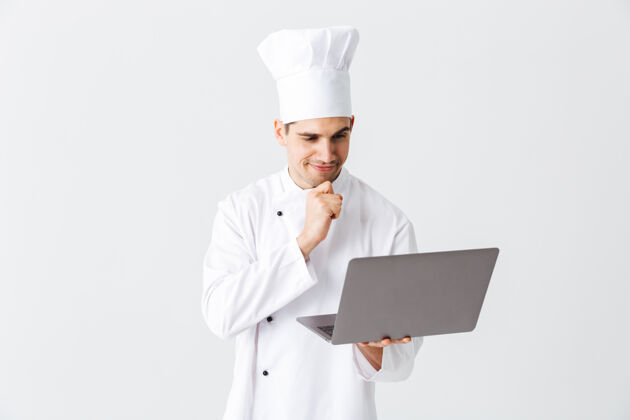 服务面带沉思的厨师身穿制服站在白色的墙上 手里拿着笔记本电脑烹饪英俊员工