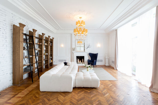 公寓豪华宽敞明亮的现代室内房间白色昂贵的沙发和木制架子 白色的墙壁和一个豪华的枝形吊灯漂亮舒适房间