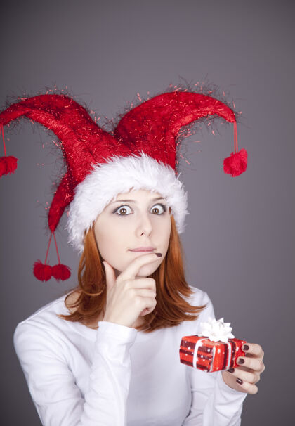 女性滑稽的红发女孩戴着圣诞帽 手里拿着礼品盒盒子坐着内衣