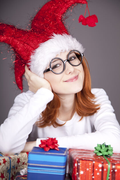 尼斯滑稽的红发女孩戴着圣诞帽 戴着带礼盒的眼镜包装盒子欢乐
