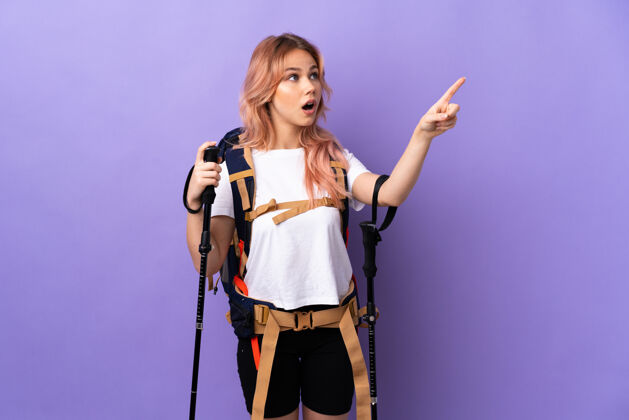 设备带着背包和登山竿的女孩在孤立的紫色上指指点点散步徒步旅行表演