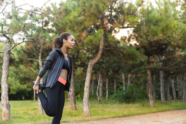 伸展一位20多岁的黑人黑人妇女身穿黑色运动服 在绿色公园里锻炼身体女性跑步听