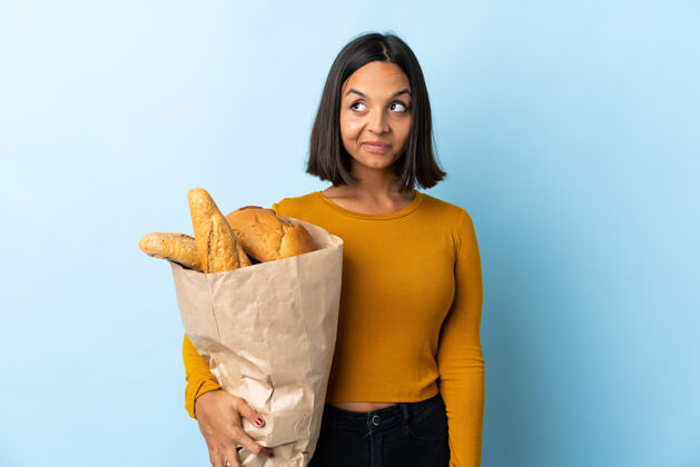 成人年轻的拉丁女人买了一些面包蓝色有疑问 而抬头看沉思表达思考