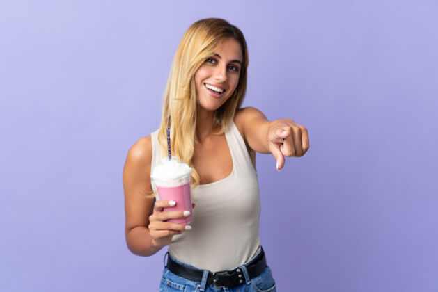 食物年轻的金发乌拉圭女人 拿着草莓奶昔孤立地站在紫色的前面 表情愉快金发甜点奶昔