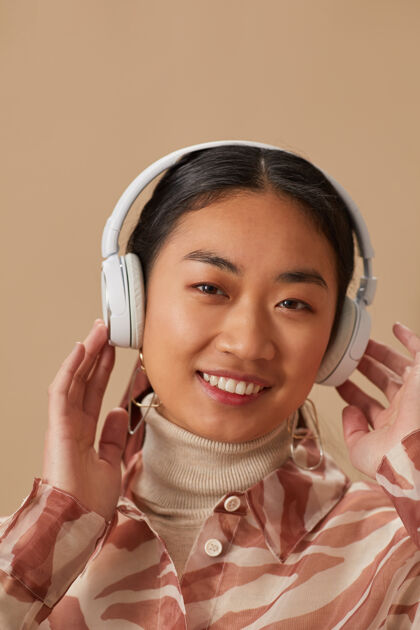 欢乐戴着无线耳机听音乐 微笑在前方的亚洲年轻女子肖像室内无线技术放松