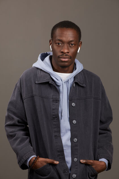 夹克戴着耳机 穿着休闲服的年轻人的肖像 在灰色的墙上看着孤立的前方态度时尚姿势