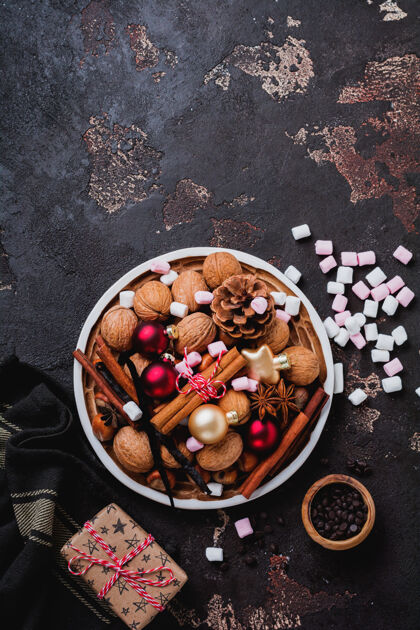 陶瓷混合健康的生榛子和核桃 肉桂棒 八角 香草 巧克力和圣诞玩具在陶瓷板上棕色混凝土表面明信片巧克力水果
