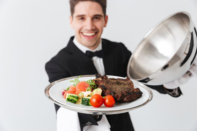 服务特写镜头：一个快乐的侍者在灰色的墙上展示一道肉菜人管家手