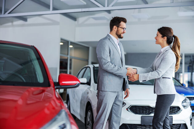 推销员友好的女汽车销售商站在汽车沙龙与顾客握手零售男性微笑
