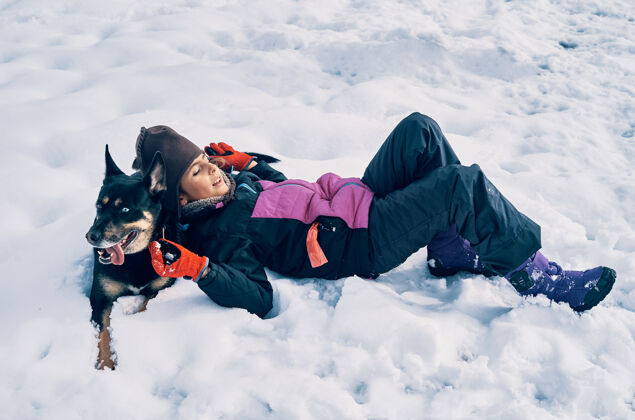 玩耍一个白人女孩非常温暖 戴着帽子和她的狗躺在雪地里寒冷狗季节
