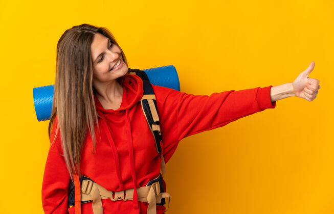 积极一位斯洛伐克登山妇女背着一个大背包 孤立地站在黄色背景上竖起大拇指女孩站立成人