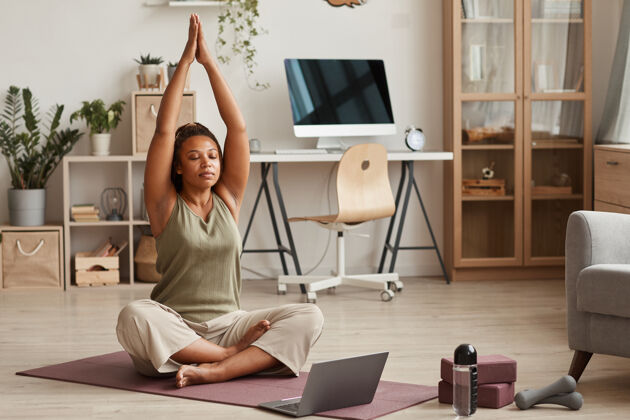 运动年轻女子坐在笔记本电脑前的运动垫上 在家里做瑜伽锻炼冥想舒适