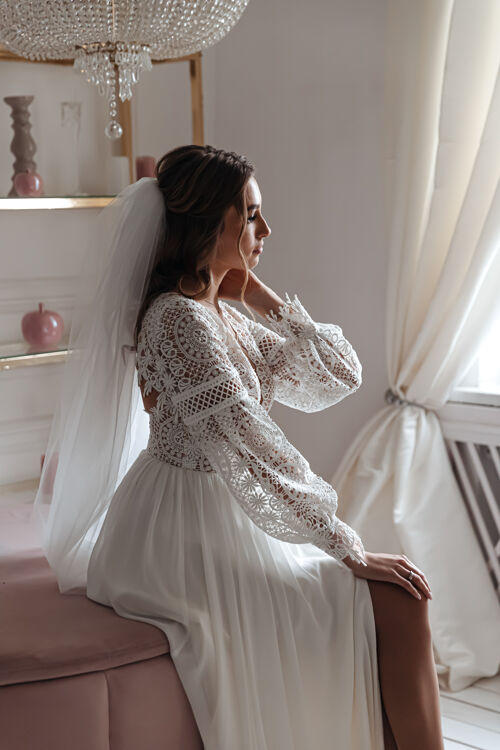 年轻新娘穿着波西米亚风格的婚纱 戴着面纱坐在舒适的房间里温柔礼服姿势
