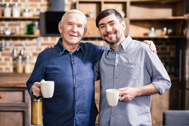 男性快乐的年迈的父亲和儿子在家喝咖啡时拥抱在一起朋友儿子健康
