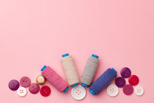 工艺粉色表面上的彩色线轴和纽扣纤维爱好针线