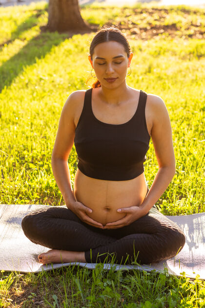 腹部安详的年轻积极的孕妇穿着体操服坐在垫子上做瑜伽和冥想怀孕运动放松
